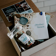 Load image into Gallery viewer, Card board box filled with book called mother beach and bag of Lake Erie Candy Company candy on a tan background.
