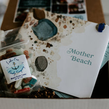 Load image into Gallery viewer, Up close shot of a card board box filled with book called mother beach and bag of Lake Erie Candy Company candy on a tan background.
