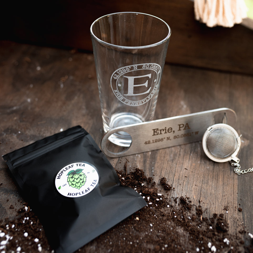 Large Erie coordinates beer stein with a bottle opener, tea strainer, bag of Hopleaf tea and dirt spread out in the background 