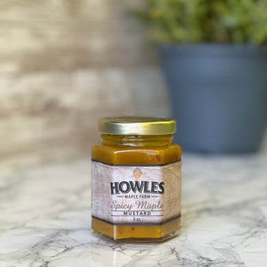 Single jar of Howles maple farm spicy maple mustard on a white marble floor with a plant in the background
