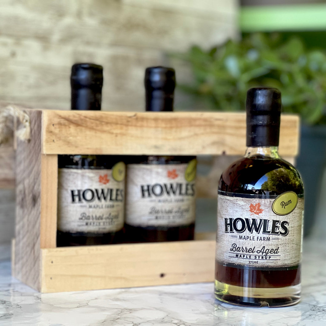 Three bottles of Howles barrel aged syrup crate pack on marble table with plant in background