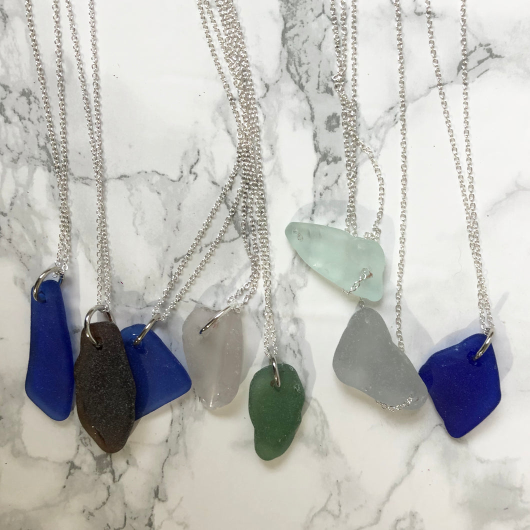 Eight Agatha & Emily Erie Beach glass necklaces on a silver chain In front of a white marble background