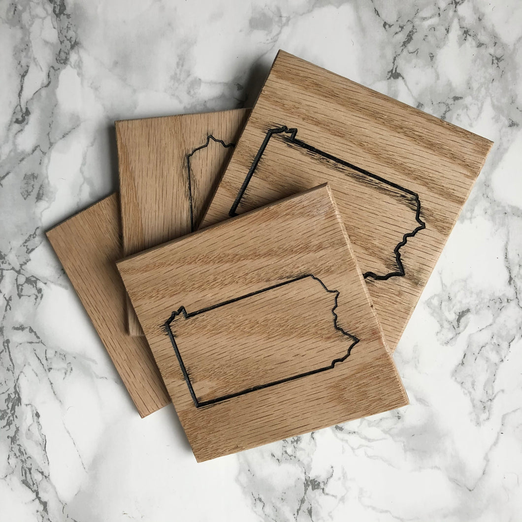 Four wooden PA shaped coasters on a white marble background