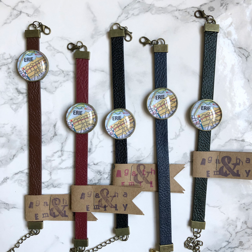 Six Agatha & Annie Erie Map Bracelets all with different colored straps in front of a white marble background