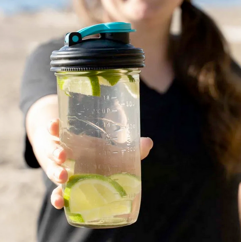 Women with brown hair holding a mason jar filled with a clear liquid and limes with a black pour cap on top of mason jar