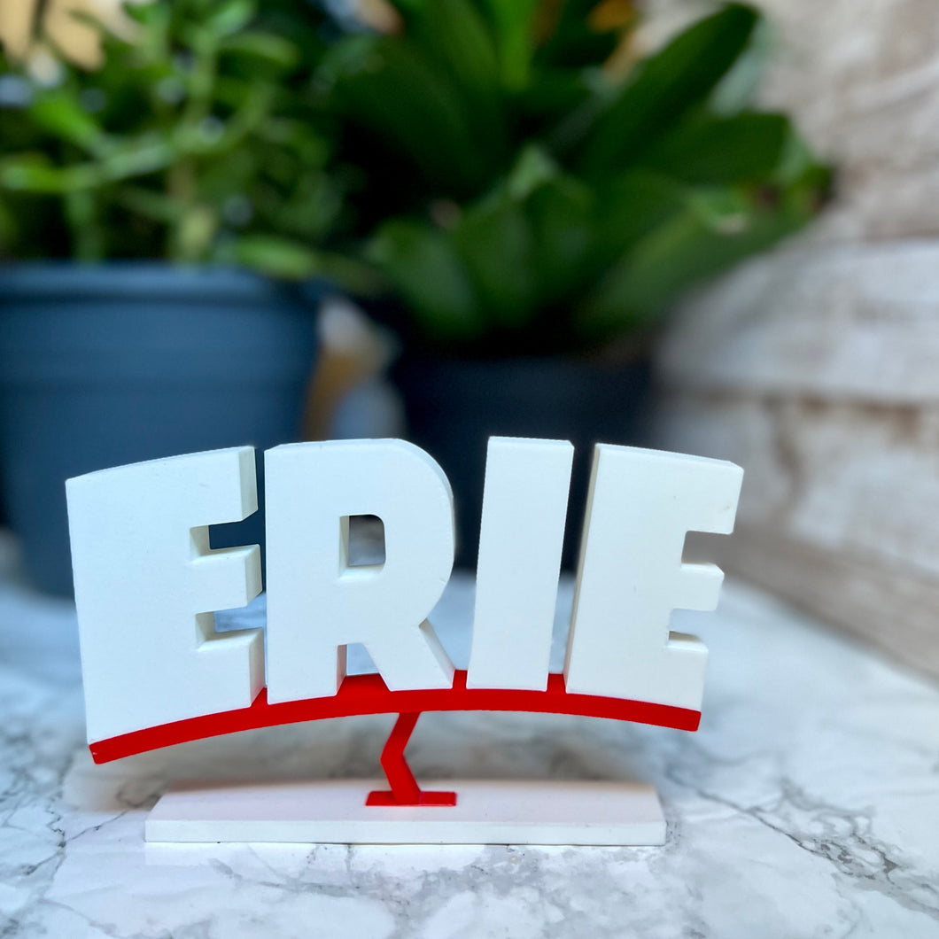 Mini white and red Erie sign on a marble background with plants in the background